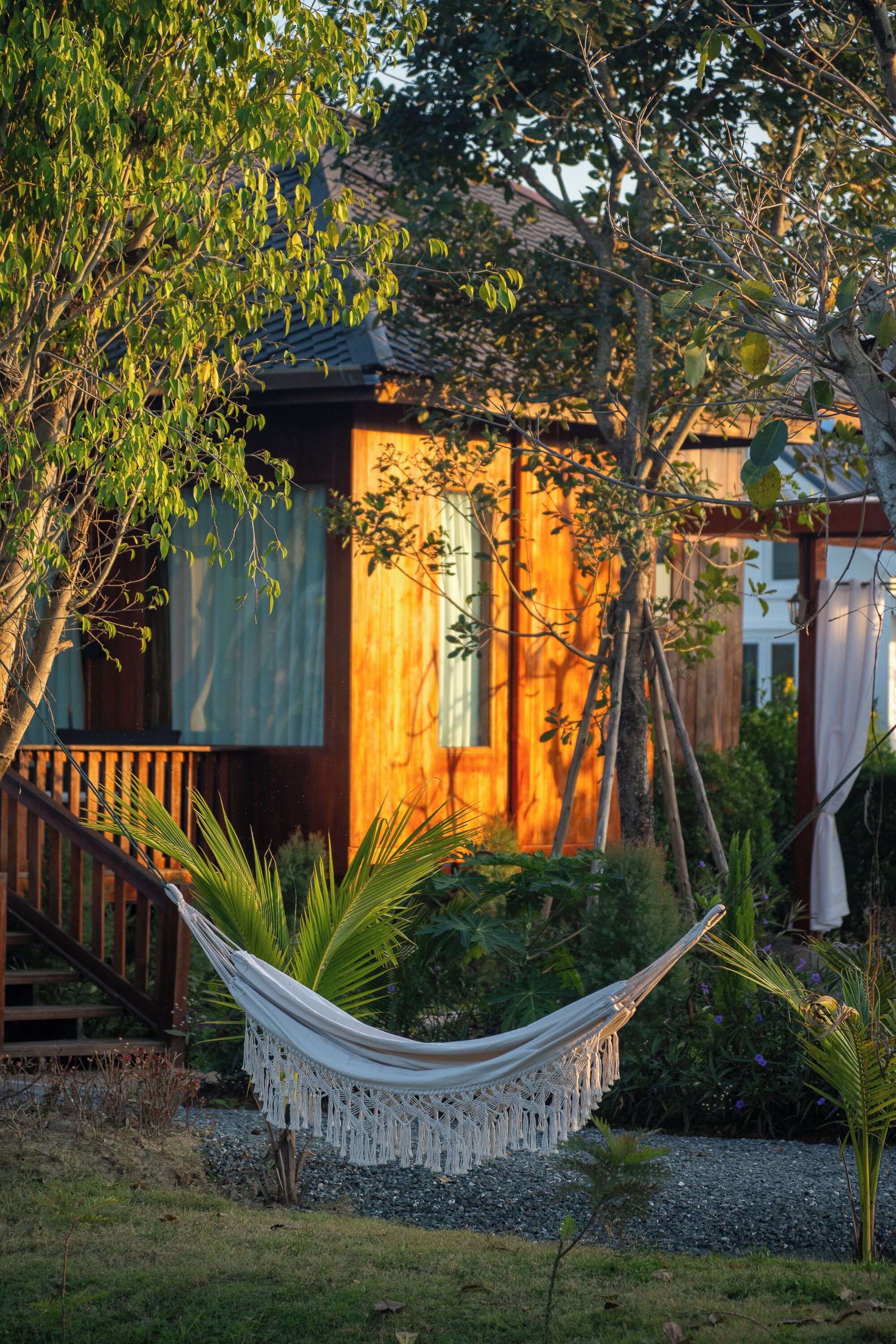 A hammock in a garden area with a wooden house in the background.
