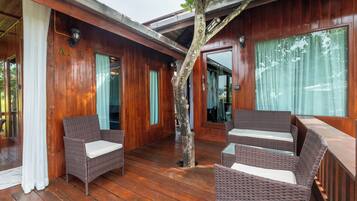 Une terrasse en bois avec des meubles en osier, un arbre et une porte vitrée.