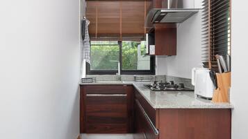 A compact kitchen with dark wood cabinets, a granite countertop, a built-in stove, and a window with blinds.