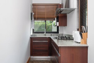 A compact kitchen with dark wood cabinets, a granite countertop, a built-in stove, and a window with blinds.