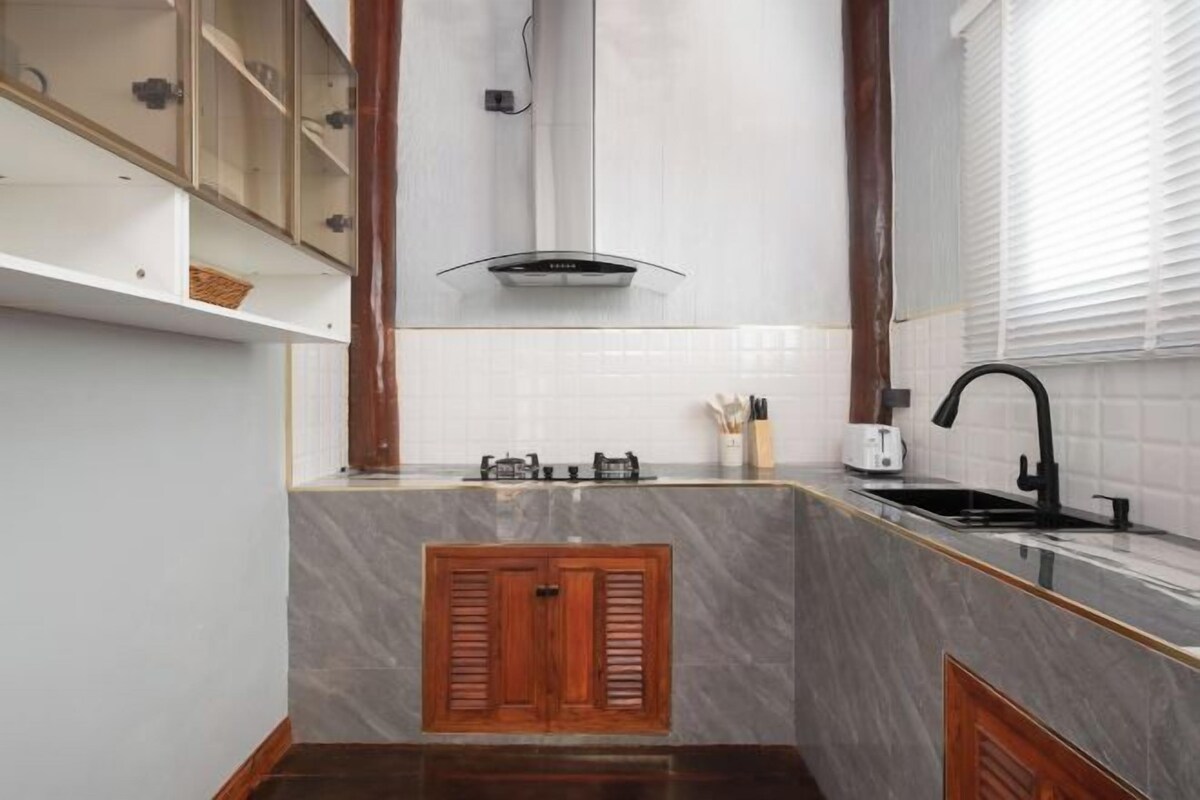 A kitchen with a marble countertop, wooden cabinets, a black faucet, and a built-in range hood.