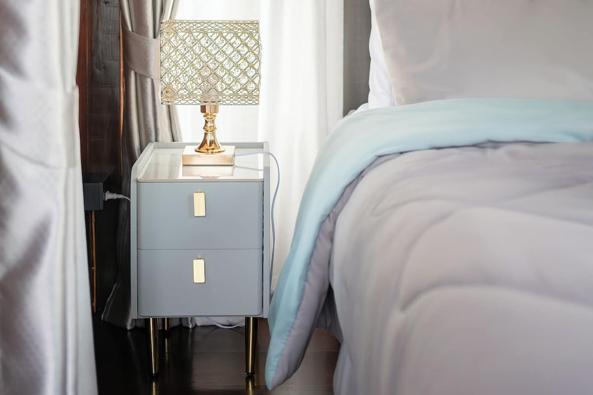 Un lit bien fait, recouvert d’une couverture bleue, une table de chevet avec une lampe et une tête de lit en bois.