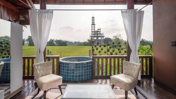 A balcony with two chairs, a glass table, and a hot tub.
