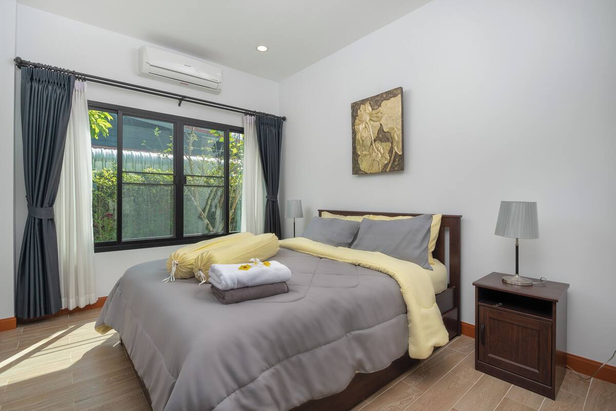 Une chambre à coucher avec un grand lit, une table de chevet avec une lampe et une fenêtre avec des rideaux.