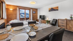 Un ambient acollidor a una cabana de muntanya, amb interior de fusta, una taula de menjador amb plats i gots, un televisor i un quadre amb una vista de muntanya a la paret.