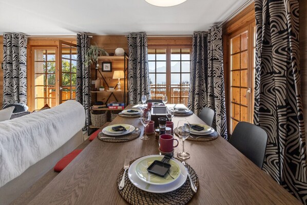 A dining area with a long wooden table set for a meal, flanked by two beds with patterned curtains.