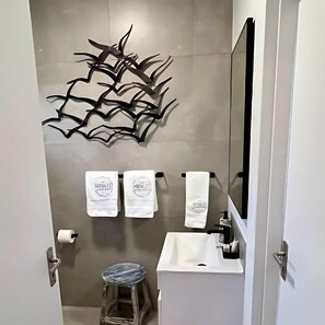 Un baño moderno con un lavamanos blanco, un espejo y dos toallas colgadas en un perchero.