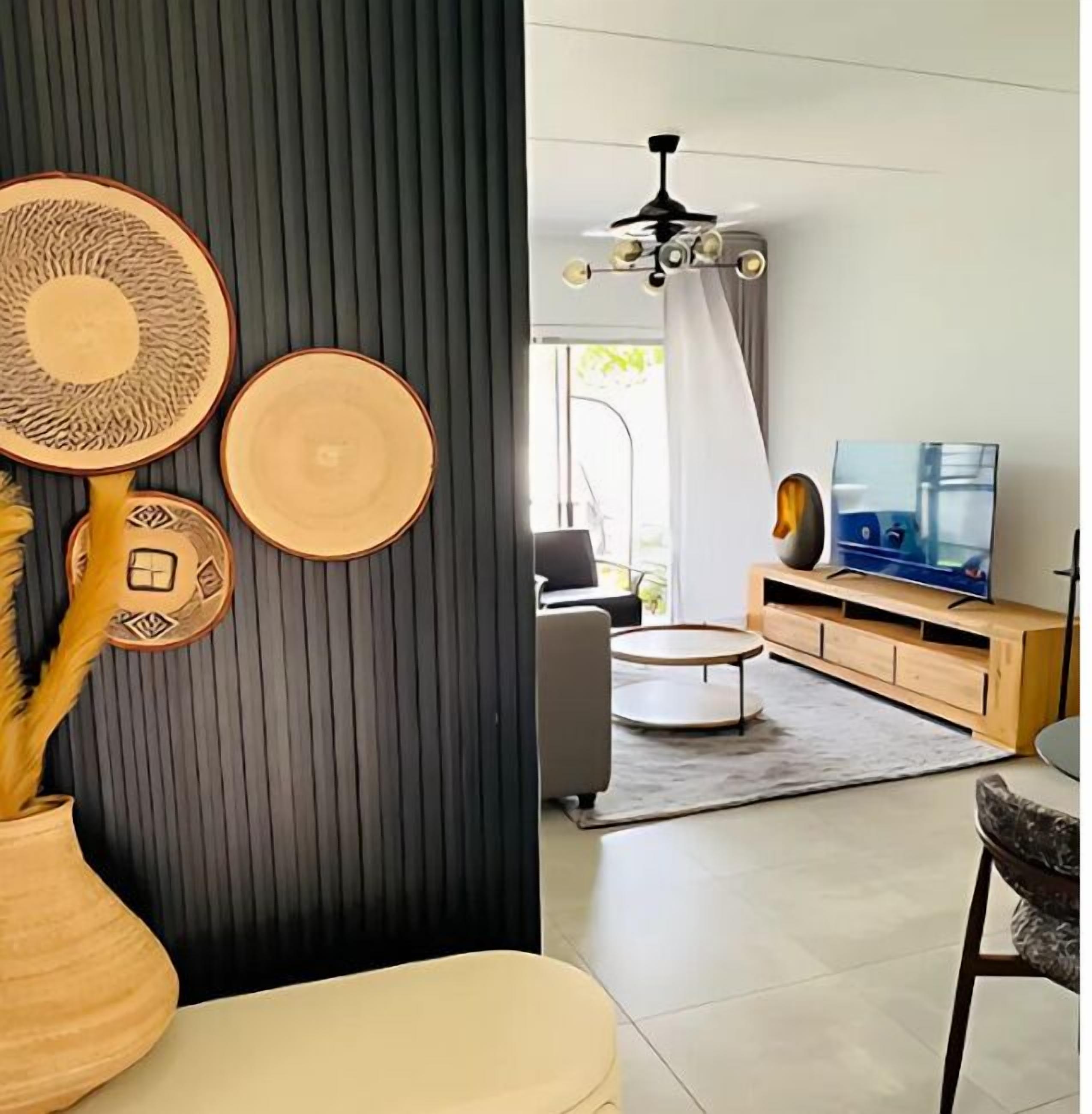 A modern living room with a black accent wall, a ceiling fan, a television, and a wooden entertainment unit.