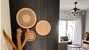 A modern living room with a dark curtain backdrop, a white bench, a vase with decorative items, and a ceiling fan. - The Henlee Apartment Tocara (Chartwell)