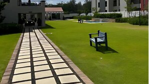 A pathway leading to a building with a pool and a bench in a grassy area. - The Henlee Apartment Tocara (Chartwell)