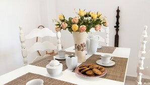 Een eettafel gedekt met wit servies, een vaas bloemen en koekjes.