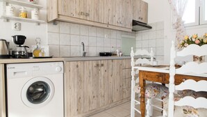 Een keuken met een wasmachine, houten kastjes, een koffieapparaat en een eethoek met een bloemenstoel.