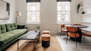 A modern living room with a green sofa, a coffee table, and a dining area with a round table and chairs. - Stylish newly refurbished 2-bed retreat in the heart of London (London)