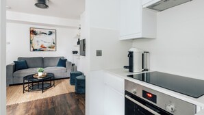 Una cucina moderna con piano cottura nero, mobili bianchi e orologio digitale che segna le 12:38.
