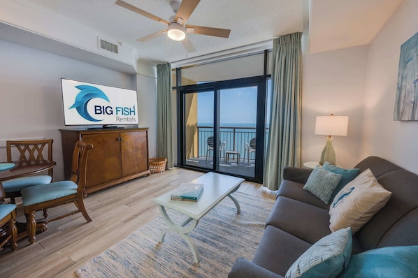 Ein geräumiges Wohnzimmer mit einem großen Flachbildfernseher, einem Deckenventilator, einem Balkon mit Blick und einem Essbereich mit Holzzimmermöbeln.