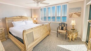 Une chambre à coucher avec un grand lit, un ventilateur de plafond, un bureau avec une chaise et une fenêtre avec des volets.