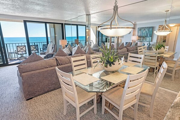 Una sala moderna con una mesa de comedor de vidrio, sillas color beige y un sofá con cojines marrones.