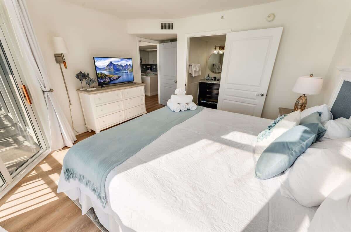 Une chambre à coucher avec un grand lit, une télévision, une commode et une salle de bain visible à travers une porte ouverte.