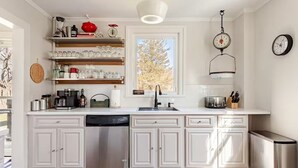 A modern kitchen with white cabinetry, a stainless steel dishwasher, a sink, and a window with a view of trees.