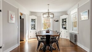 A dining room with a wooden table and chairs, a chandelier, and white cabinetry.