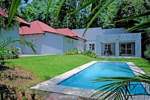 A modern house with a swimming pool, surrounded by lush greenery and a well-maintained lawn.