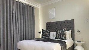 Camera da letto con un letto grande, tende grigie, una testiera capitonata e una lampada da comodino.
