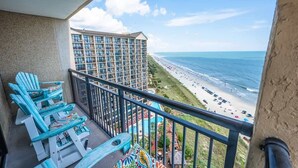 A balcony with blue Adirondack chairs overlooking a beach and a hotel building. - New Remodeled, Corner Oceanfront Beach Cove, Pools (North Myrtle Beach)