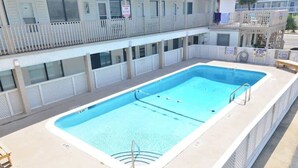A rectangular pool with a white deck, surrounded by a white fence and a balcony with a white railing.