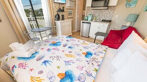 A hotel room with a bed, a small kitchenette, a dining table, and a balcony.