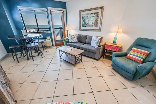 A living room with a sofa, a coffee table, a chair, a dining table with chairs, and a painting on the wall.