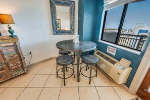 A small dining area with a round table and three stools, a mirror, a heater, and a view of the city through a window.