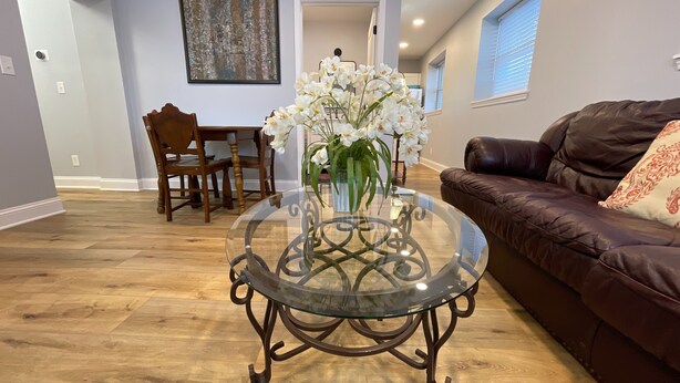 A living room with a glass coffee table, a brown leather sofa, and a dining area with wooden chairs and a table.