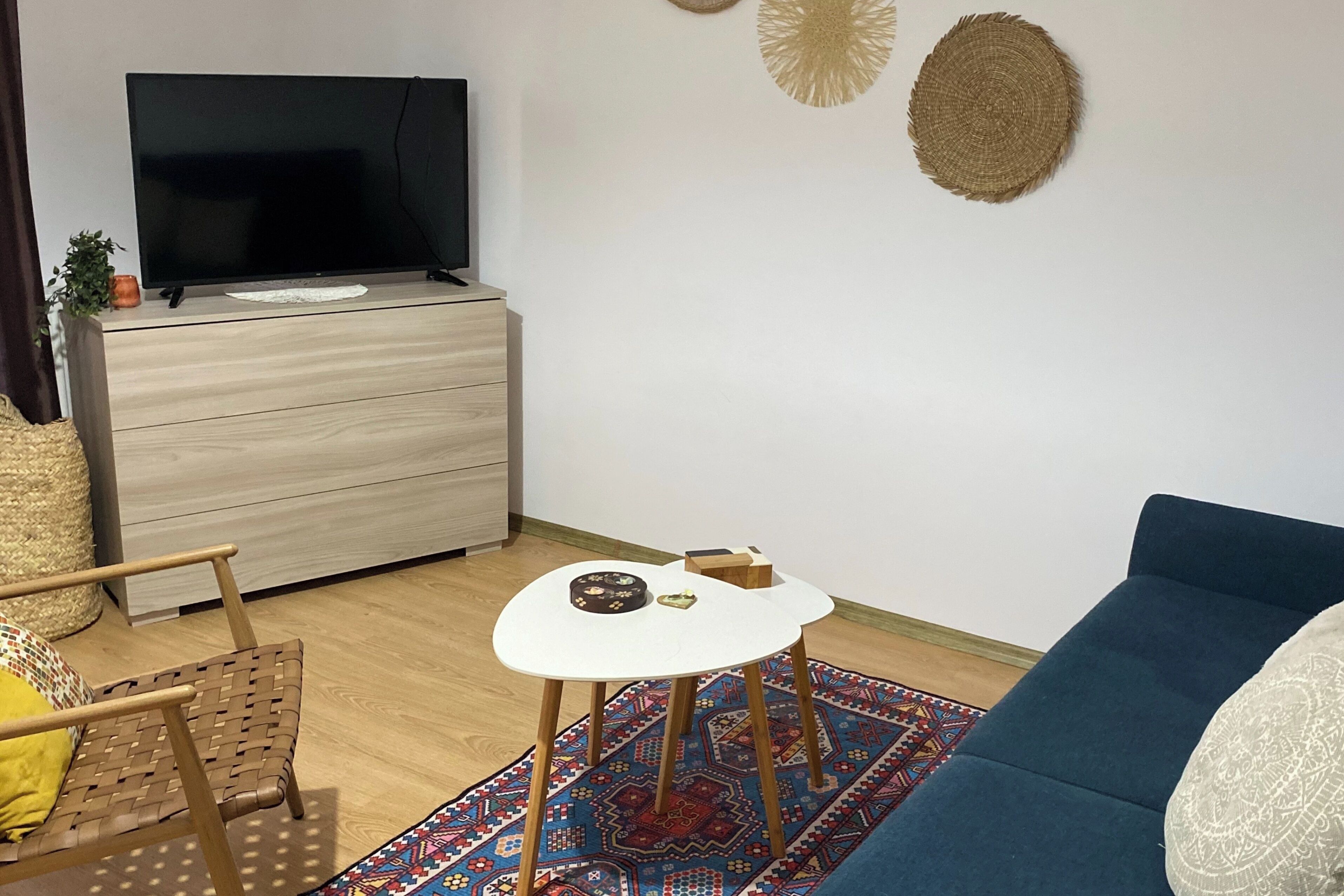 Ein Wohnzimmer mit Fernseher, Holzmöbeln, einem gemusterten Teppich und einem blauen Sofa.