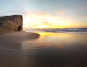 Una playa con una gran formación rocosa y una abertura parecida a una cueva.