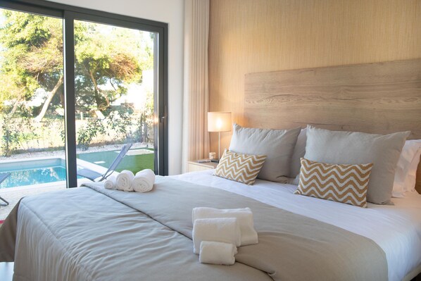 Habitación de hotel con una cama grande, vista a la piscina y cabecero de madera.