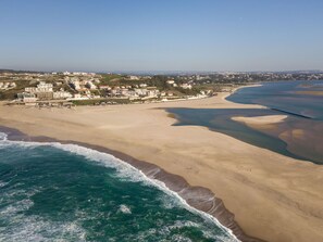 Vista aérea de una zona costera con una playa de arena, una extensa masa de agua y una área urbana densamente construida con edificios.