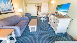 A hotel room with a sofa, a small table, a TV, a dresser, and a patterned carpet. - Direct Oceanfront, Newly Remodeled & Heated Pools! (Myrtle Beach)