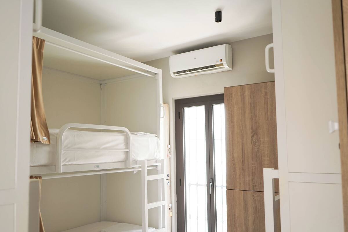 Un dormitorio con literas, una ventana, un equipo de aire acondicionado y un armario de madera.