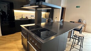 A modern kitchen with a central island, stainless steel appliances, and a bar area with stools. - Sweet Sevilla Hostel  (Seville)