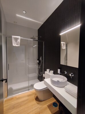 A modern bathroom with a glass shower enclosure, a white sink, and a toilet. - Sweet Sevilla Hostel  (Seville)