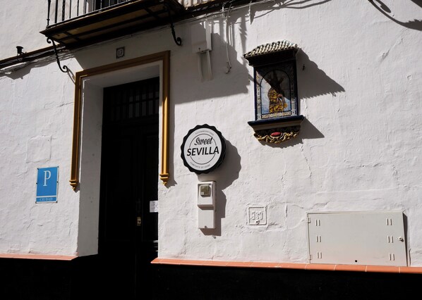 A building with a white facade, a door with a black frame, a sign reading "Sweet Sevilla", and a blue parking sign. - Sweet Sevilla Hostel  (Seville)