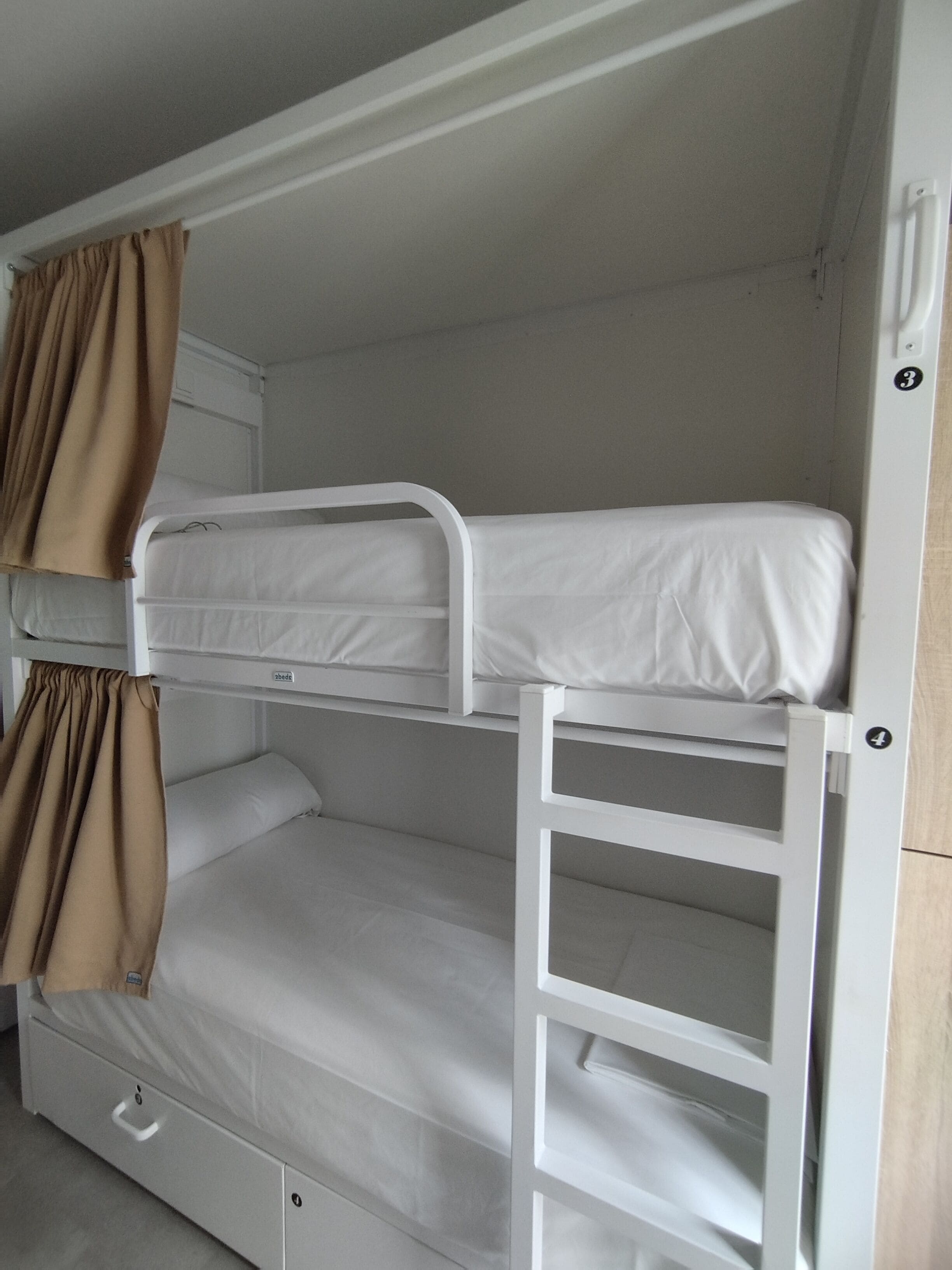 Una cama litera con escalera, un cajón pequeño y una cortina.