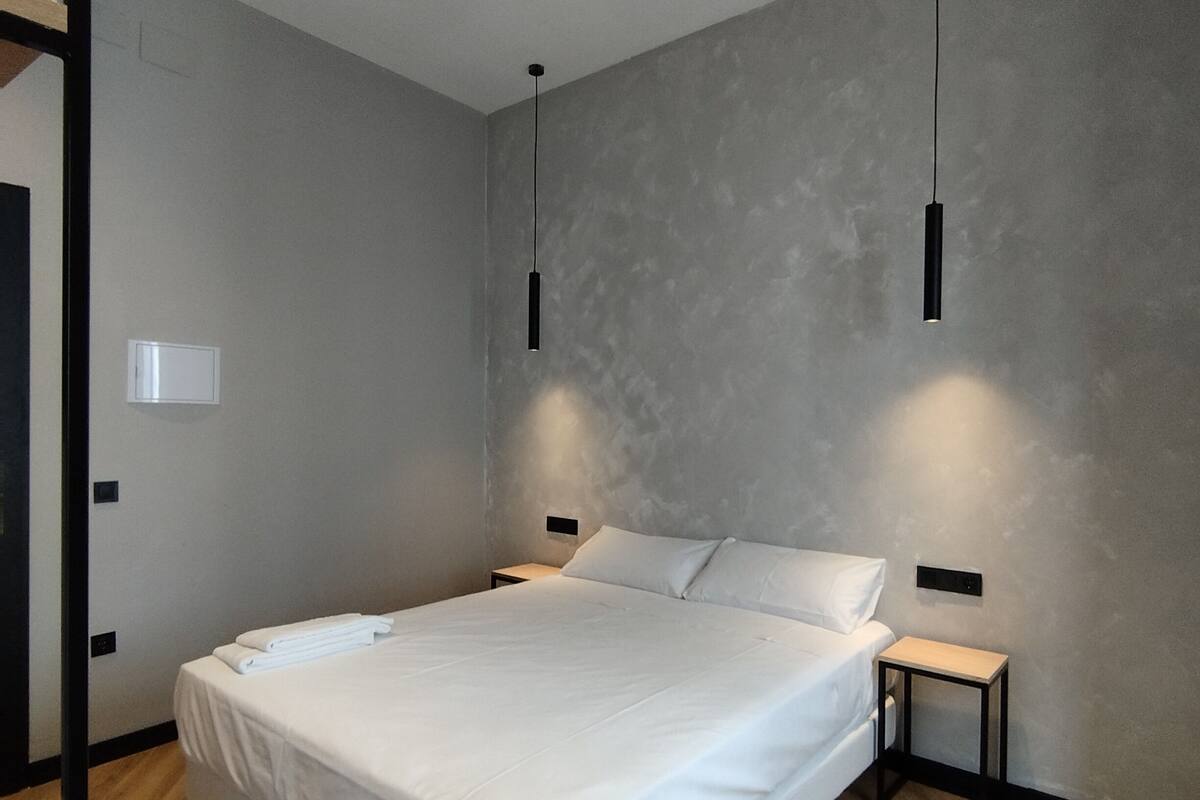 Un dormitorio moderno con una cama grande, dos mesitas de noche y lámparas colgantes.