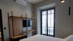 A modern bedroom with a large bed, built-in shelving, a TV, and a window with a view. - Sweet Sevilla Hostel  (Seville)
