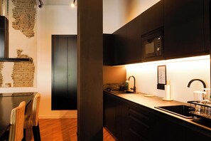 A modern kitchen with dark cabinetry, a stainless steel sink, and a microwave. - Sweet Sevilla Hostel  (Seville)