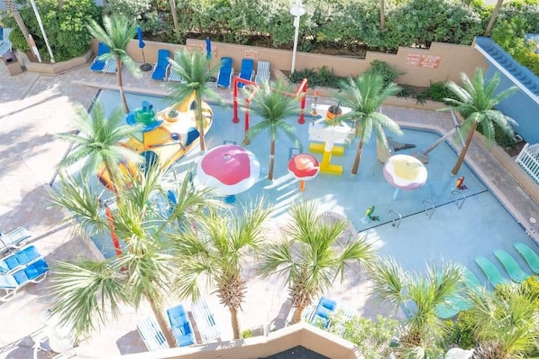 Un espace piscine agrémenté de palmiers, de chaises longues et d’une aire de jeux pour enfants.