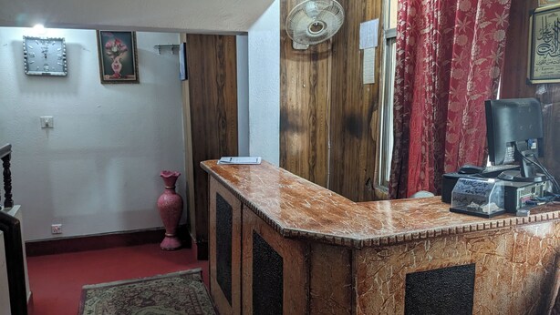 Une pièce avec un meuble en bois, un ventilateur, un rideau rouge et une petite table sur laquelle se trouve un ordinateur.