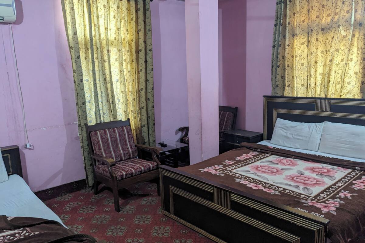Une chambre à coucher comprenant un lit, deux chaises, un bureau et un climatiseur fixé au mur.
