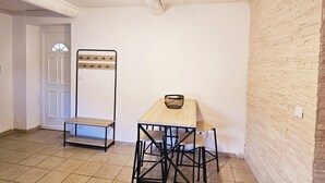 Una habitación con piso de baldosas, una mesa de madera con sillas, una puerta blanca y una pared de ladrillo.