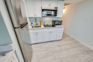 A compact kitchen with white cabinets, a stainless steel refrigerator, a microwave, and a toaster.
